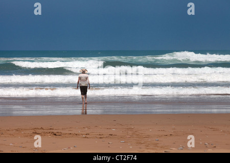 Eine Frau stand am Rande des Atlantischen Ozeans am Strand in der Nähe von Agadir, mit Füßen im Meer, Marokko Afrika Stockfoto