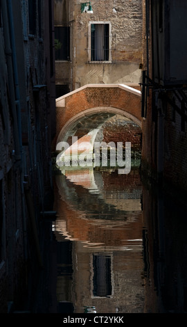 Eine Fußgängerbrücke spiegelt sich in einem ruhigen Kanal in den Seitenstraßen von Venedig, Italien Stockfoto