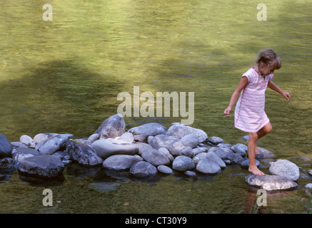 Ein junges Mädchen auf einige Flusssteine überspringen. Stockfoto