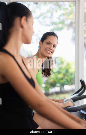 Junge Frauen reden und lachen während der Arbeit am Heimtrainer im Wellnessclub Stockfoto