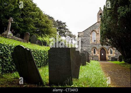 HARLECH, Wales – Ein Schotterpfad schlängelt sich durch verwitterte Grabsteine auf dem Friedhof der St. Tanwg's Church in Harlech, an der Nordwestküste von Wales. Die historische Kirche, eingebettet in die Region Snowdonia, steht am Ende des Weges, ihre Steinmauern zeugen von jahrhundertelanger walisischer religiöser Tradition und dem Leben an den Küsten. Stockfoto