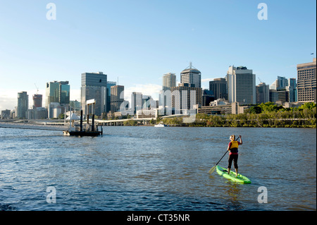 Eine Frau tun Stand-Up Paddeln am Brisbane River mit der CBD, Queensland, Australien Stockfoto