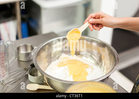 Eine Frau misst in Apfel Saucen, wie sie zusammen Zutaten in eine große Rührschüssel geben mischt während des Backens Krapfen bei Tandmen Doug Stockfoto