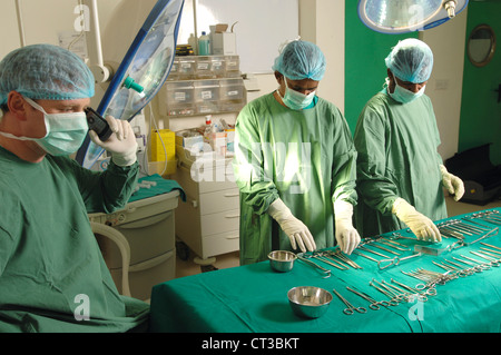 Chirurgische Theater Personal verschiedene chirurgische Werkzeuge auf dem OP-Tisch auslegen, während der Chirurg auf seinem Handy spricht. Stockfoto