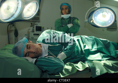 Ein unbeeindruckt Student Arzt starrte sein Arbeitskollege, als er auf einem Operationstisch schläft. Stockfoto