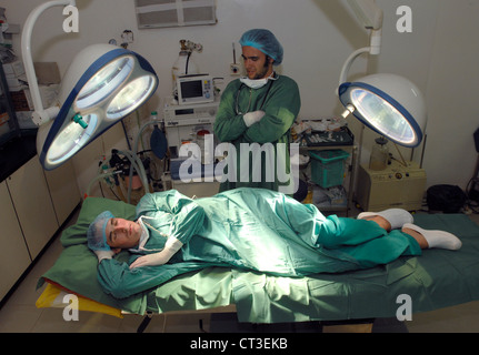 Ein Arzt unbeeindruckt Student Uhren auf, wie sein Kollege auf einem Operationstisch schläft. Stockfoto