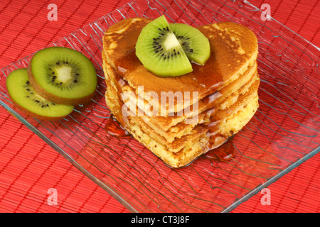 Herzförmige Pfannkuchen mit Sirup und Kiwi Frucht auf eine transparente Glasschale zum Valentinstag Frühstück. Stockfoto