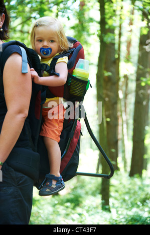 Eine Frau trägt ihre Tochter Baby Mädchen in einem Rucksack Sommer Wald Stockfoto