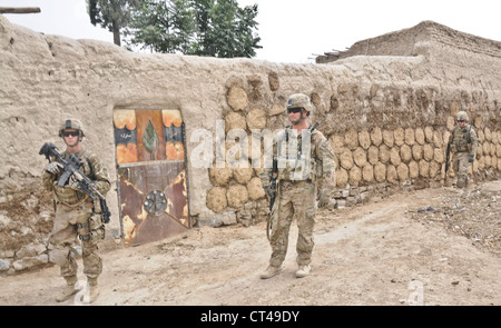 Fallschirmjäger des 3. Platoon, Alpha Battery, 2. Bataillon (Airborne), 377. Parachute Field Artillery Regiment, führen eine Sicherheitspatrouille vor einem Qalat, der mit abgedunstem und getrocknetem Kuhmist bedeckt ist, 7. Juli 2012. In den Dörfern der Provinz Khowst wird Kuhdung oft mit Stroh gemischt und getrocknet und als Brennstoff oder Biogas zur Wärmeerzeugung verwendet. Stockfoto