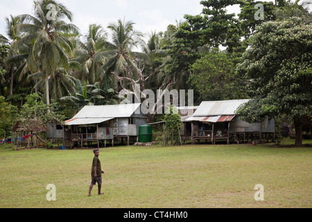 Indonesien, Papua Neu Guinea, Kitava Island. Mann zu Fuß in Richtung Gehäuse Strukturen inmitten von Palmen. Stockfoto