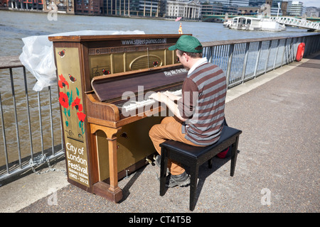 Drei Viertel Rückansicht eines Straßenmusikers, der ein altes Klavier spielt, South Bank, London, England, Großbritannien. Stockfoto