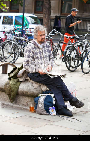In voller Länge Portrait von einem Obdachlosen sitzen und halten eine Zeitung, London, England, UK Stockfoto