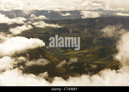 Aus der Vogelperspektive wird eine zerklüftete Berglandschaft mit tiefen Tälern, gewundenen Flüssen und grünen Feldern erfasst. Dicke weiße Wolken verdecken teilweise das Gelände und treiben Stockfoto