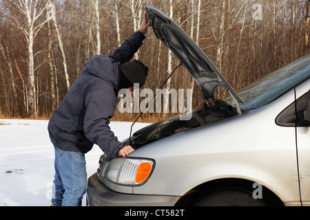 Mann sucht unter der Haube eines Fahrzeugs im Winter. Stockfoto