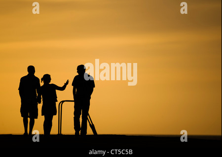 Ein Sommerabend: Menschen Silhouette bei Sonnenuntergang zu Fuß entlang der Mole am Hafen von Aberystwyth, Wales UK Stockfoto