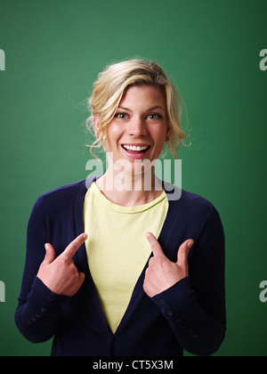junge Frau zeigt sich vor grünem Hintergrund und Blick in die Kamera Stockfoto