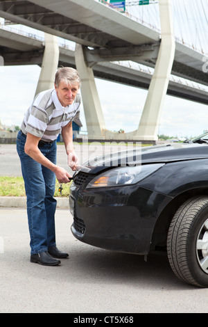 Ältere russische Fahrer versucht vor Fahrzeug Motor Fach Haube steht zu öffnen Stockfoto