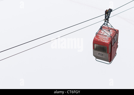 Alte rote Seilbahn hängend auf Berg mit Schnee bedeckt. Stockfoto