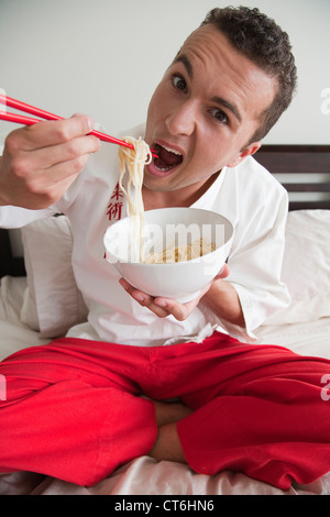 Porträt eines jungen Mannes, der eine Schüssel Nudeln mit Stäbchen zu essen Stockfoto