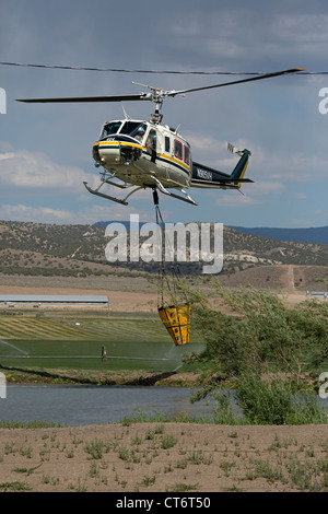 Ein Feuerwehrmann Hubschrauber eilt um zu helfen, ein Lauffeuer, tragen einen großen Eimer mit Wasser zu löschen. Stockfoto