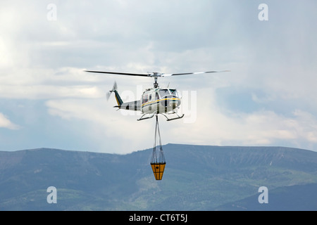 Ein Feuerwehrmann Hubschrauber eilt um zu helfen, ein Lauffeuer, tragen einen großen Eimer mit Wasser zu löschen. Stockfoto