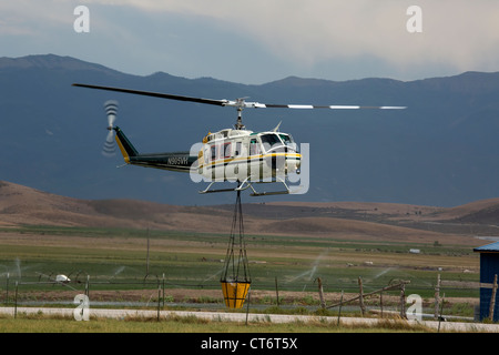 Ein Feuerwehrmann Hubschrauber eilt um zu helfen, ein Lauffeuer, tragen einen großen Eimer mit Wasser zu löschen. Stockfoto