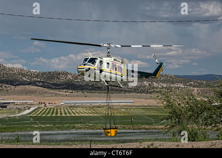 Ein Feuerwehrmann Hubschrauber eilt um zu helfen, ein Lauffeuer, tragen einen großen Eimer mit Wasser zu löschen. Stockfoto