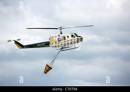 Ein Feuerwehrmann Hubschrauber eilt um zu helfen, ein Lauffeuer, tragen einen großen Eimer mit Wasser zu löschen. Stockfoto