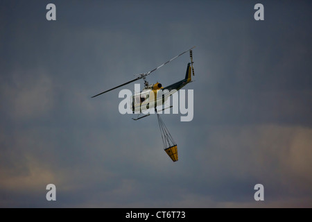 Ein Feuerwehrmann Hubschrauber eilt um zu helfen, ein Lauffeuer, tragen einen großen Eimer mit Wasser zu löschen. Stockfoto