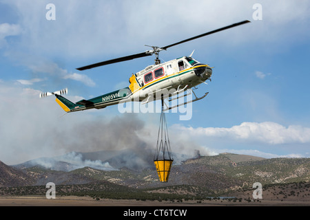 Ein Feuerwehrmann Hubschrauber eilt um zu helfen, ein Lauffeuer, tragen einen großen Eimer mit Wasser zu löschen. Stockfoto