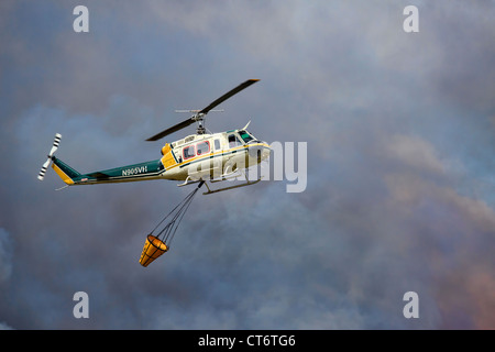 Ein Feuerwehrmann Hubschrauber eilt um zu helfen, ein Lauffeuer, tragen einen großen Eimer mit Wasser zu löschen. Stockfoto