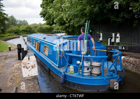 Ein Mann navigiert seinen engen Schiff durch eine Schleuse entlang der Grand Union Canal in Watford, England. Stockfoto