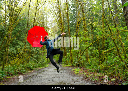 Springende Frau im Wald mit roten Regenschirm Stockfoto