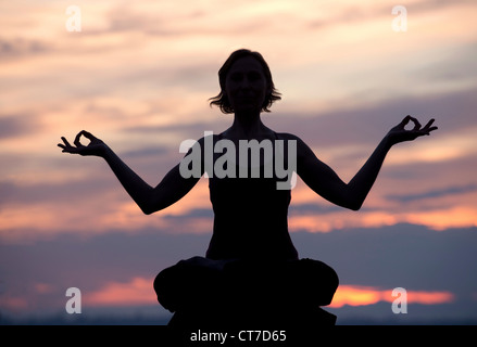 Silhouette der Frau im Lotussitz bei Sonnenuntergang Stockfoto