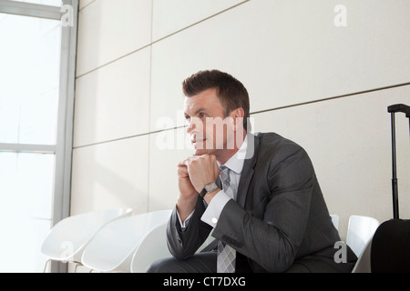 Geschäftsmann wartet mit Gepäck, hand aufs Kinn Stockfoto