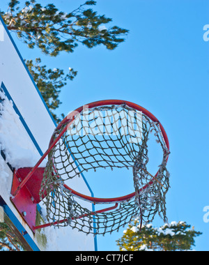 Basket ball Ring mit einem teilweise zerrissen Net und einem blauen Himmel im Hintergrund Stockfoto