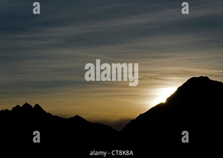 Die untergehende Sonne hinter einem Alpenkamm Stockfoto