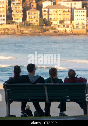 Zwei Frauen und zwei Männer in frühen 20ern auf Bank mit Blick auf Bondi Beach bei Sonnenuntergang Sydney New South Wales Australien Stockfoto