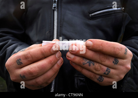 Nahaufnahme von zwei Hände mit Tattoos auf den Fingern rollt eine Zigarette mit losen Tabak, Govan, Glasgow, Scotland, UK Stockfoto