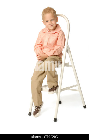 Süße, blonde fünf Jahre alter Junge sitzt auf einer Trittleiter. Kaukasischer Ethnie. Er ist Khaki-Hosen und ein Hemd tragen. Stockfoto