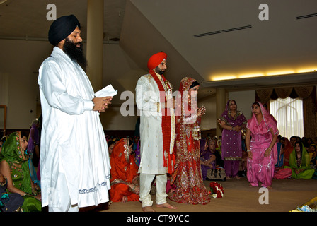 Traditionellen indischen Heiligen Mann Bräutigam Braut Hochzeit Hochzeitsgast sitzend Schneidersitz auf Boden Sikh-Tempel Stockfoto