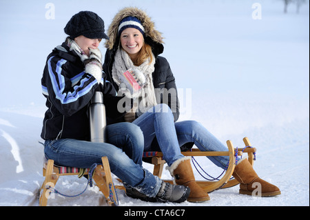 Zwei junge Frauen auf einem Schlitten sitzen und ausruhen, Tal Leitzachtal, Upper Bavaria, Bayern, Deutschland, Europa Stockfoto