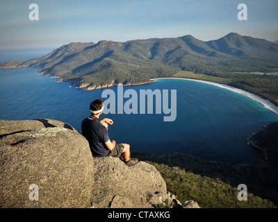 Wanderer genießt Aussicht von einem Felsen auf Mt Amos am Wineglass Bay, Strand, Freycinet National Park, Tasmanien, Australien Stockfoto