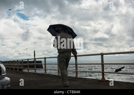 Mann mit einem Regenschirm, ein Spaziergang entlang der Strandpromenade Stockfoto