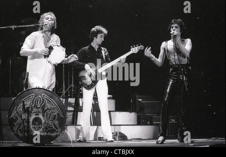 Queen treten live im Hammersmith Odeon in London im Dezember 1975 während der A Night at the Opera-Tour auf. Roger Taylor spielt Tamburin und singt neben Bassist John Deacon, während Freddie Mercury am Mikrofon auftritt. Stockfoto