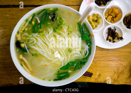 Eine Schüssel frische / authentische / echte chinesische Nudelsuppe mit einem traditionellen Suppenlöffel in einem Restaurant in Peking, China. Nudeln scheinen aus Reis zu sein. Stockfoto