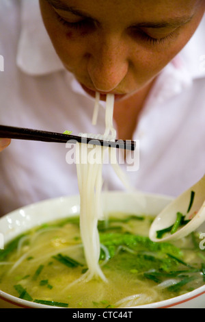 Westliche Frau Tourist essen frische / authentische / echte chinesische Reisnudeln Suppe mit Stöcken in einem Restaurant in Peking, China. Stockfoto