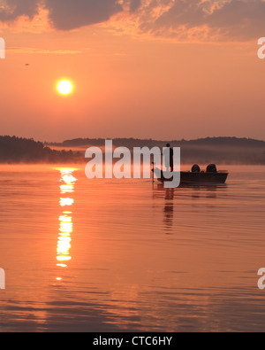 Fischer in einem Boot gegen eine aufgehende Sonne. Stockfoto