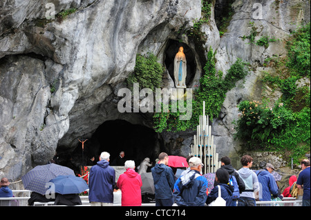 Pilger im Regen beten vor der Grotte an der Wallfahrtskirche unserer lieben Frau von Lourdes, Pyrenäen, Frankreich Stockfoto