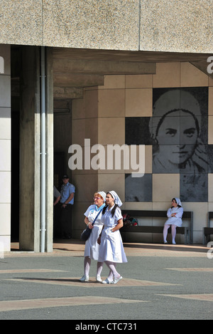 Krankenschwestern vor der Basilika des heiligen Pius X / unterirdische Basilika an der Wallfahrtskirche unserer lieben Frau von Lourdes, Pyrenäen, Frankreich Stockfoto